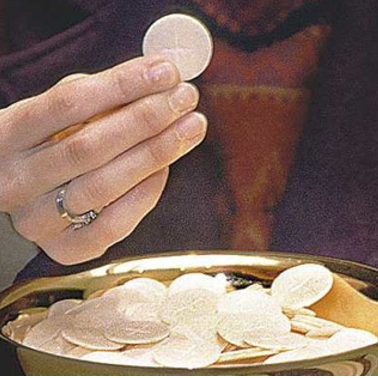 Hand holding a Communion host over a bowl of hosts